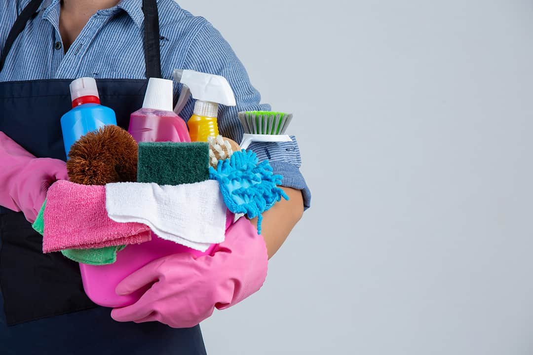 Woman wearing apron and holding cleaning products in bucket against white background