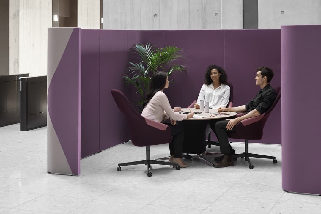 Two women and a man having a conversation sat at a circular table surrounded by purple walls in building