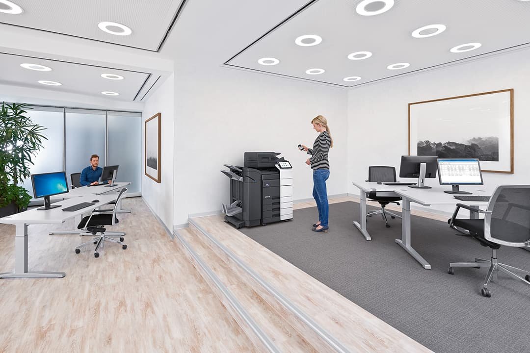 Large open white modern office with lady using printer and man sat at desk using computer