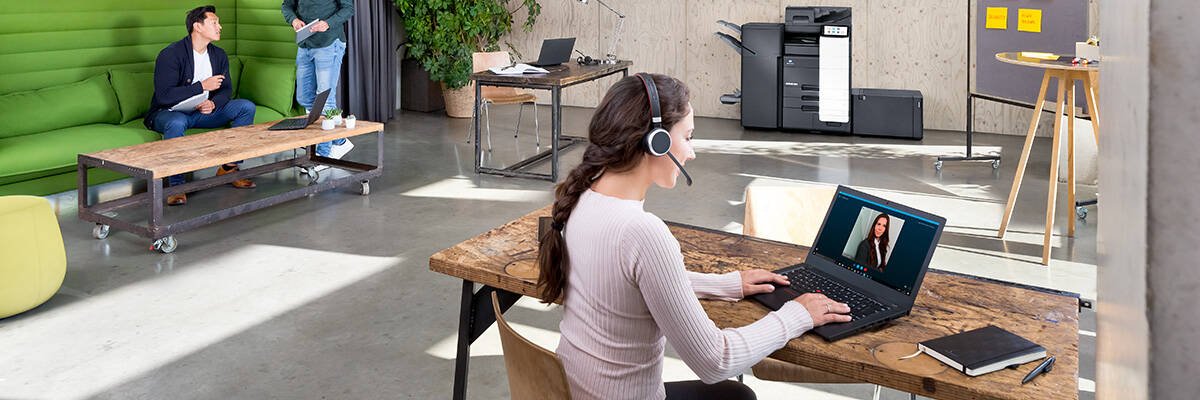 Lady sitting at a wooden desk using laptop with headset on in office environment