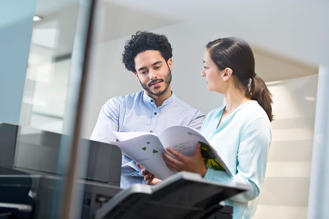 Man and a woman looking through a booklet and stood by the printer