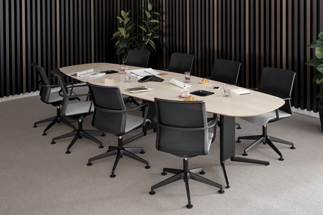 Simple meeting room with wooden table and eight office chairs and plants in corners