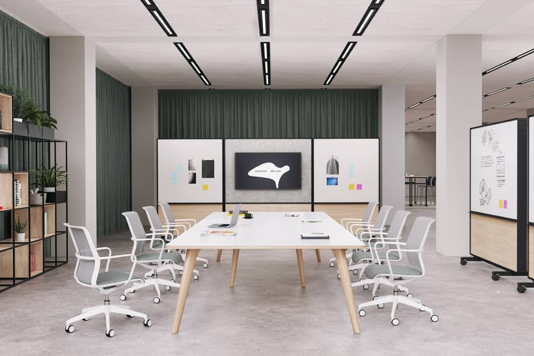 Light meeting room with large table and 8 grey chairs on either side surrounded by presenting boards and decor