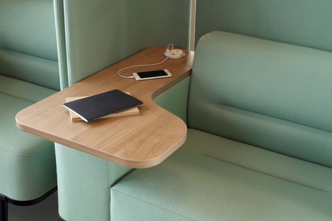 Closeup of pastel green armchair with wooden armrest with charging point, phone and two notepads