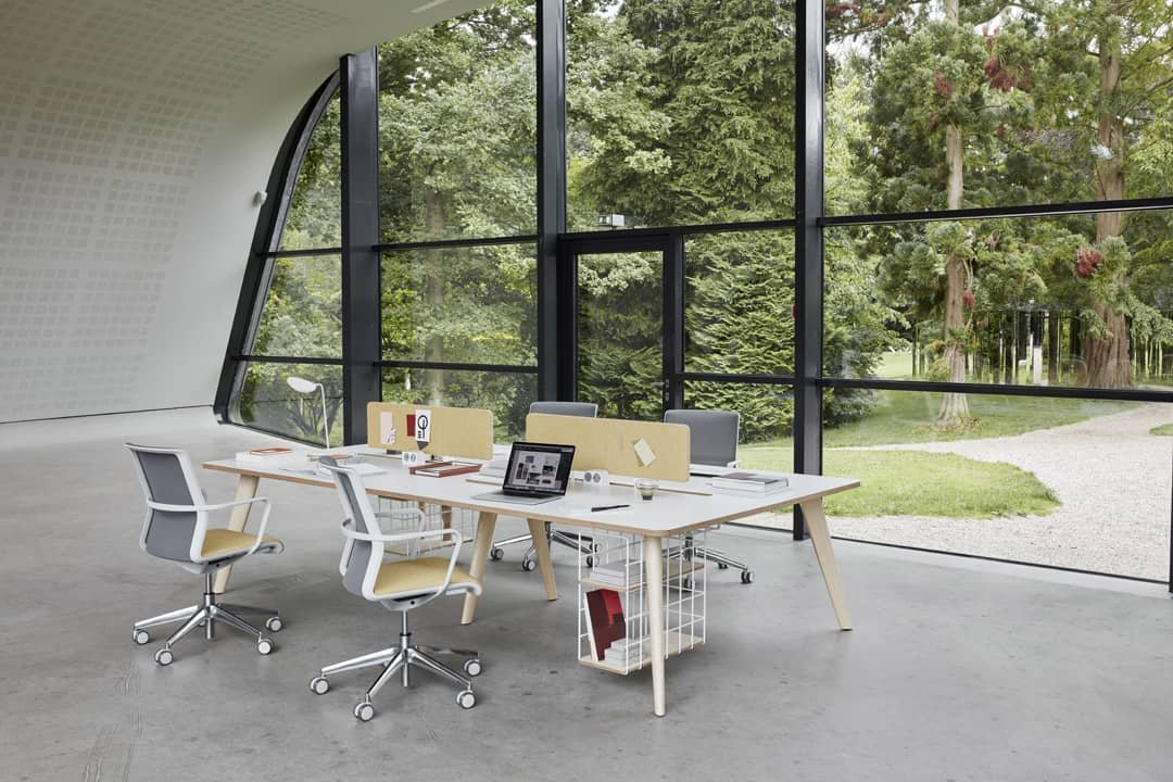 Large open room with one office desk and four chairs with large glass panel and trees outside