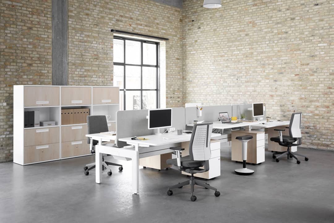 White office desks with white office chairs and computers in a rustic minimal brick office setting