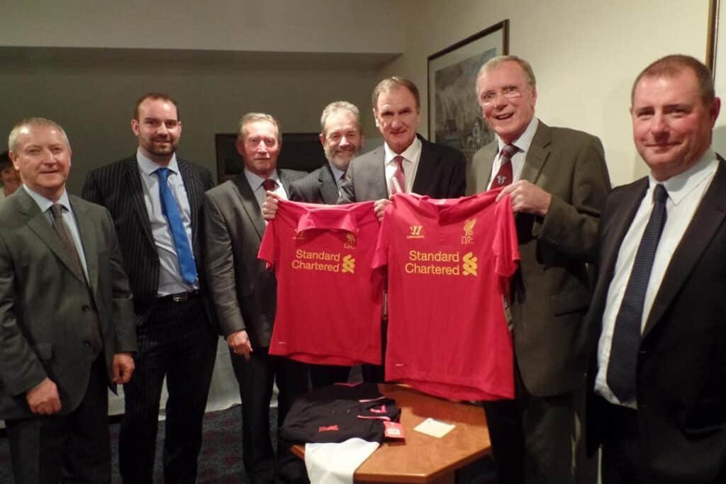 Group of men in suits holding Liverpool football shirts