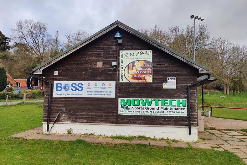 A small wooden clubhouse in a field, promoting the BOSS banner.