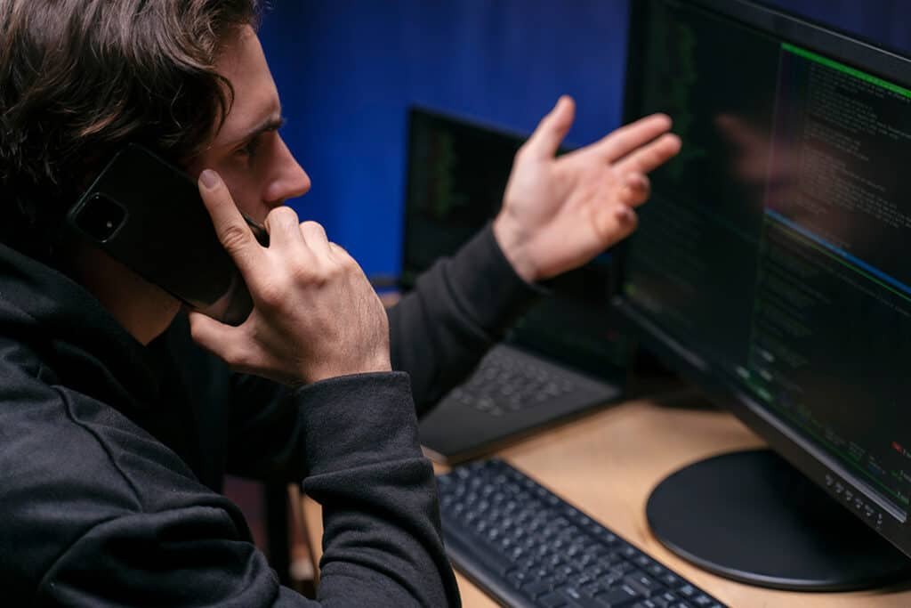 A man on the phone discussing something whilst looking at the computer