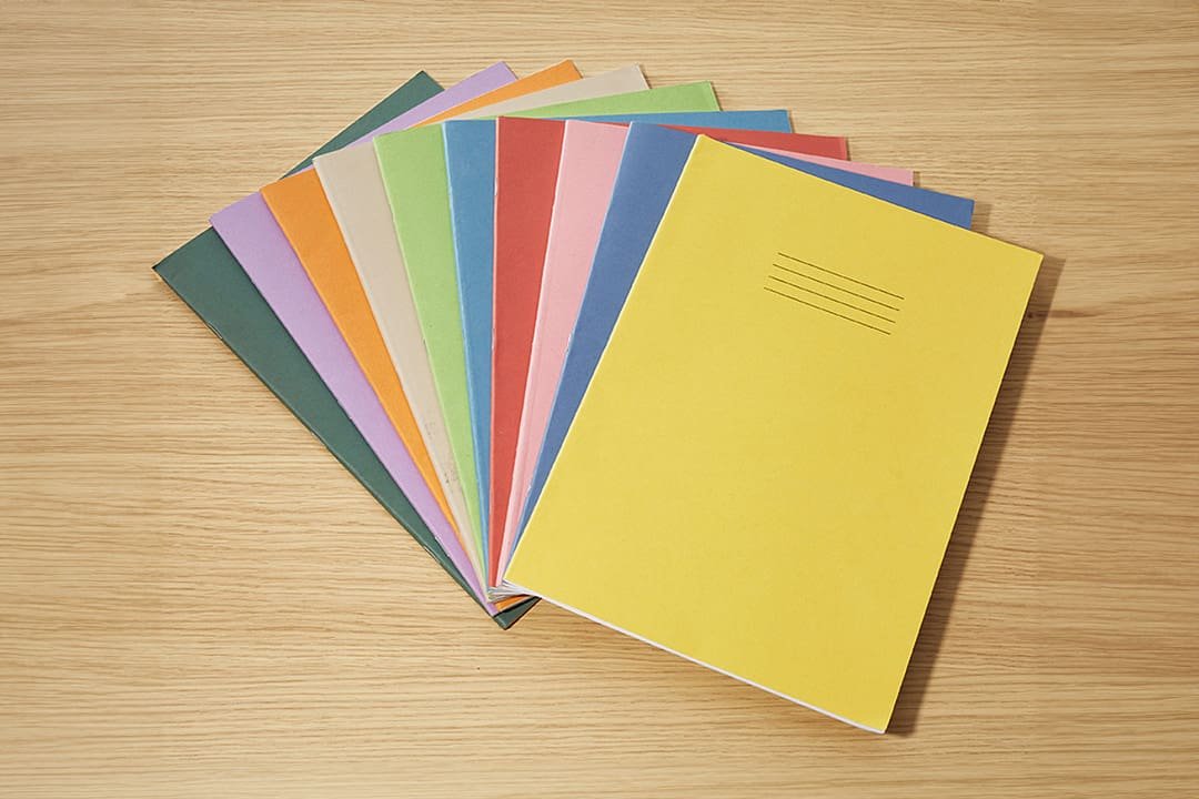 Coloured exercise books stacked against wooden surface